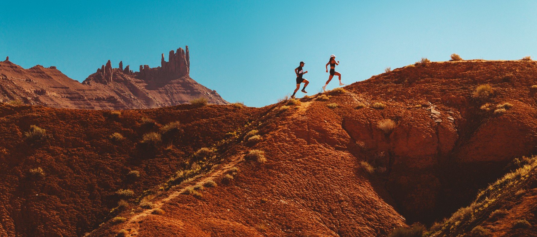 Two runners on a red desert ridge wearing Merrell Speed Strike 2 shoes